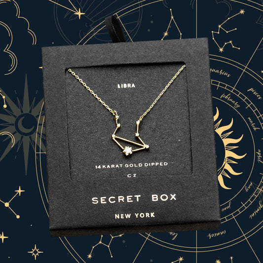 Gold-dipped Libra constellation necklace in a 'Secret Box New York' packaging against a starry night sky background.